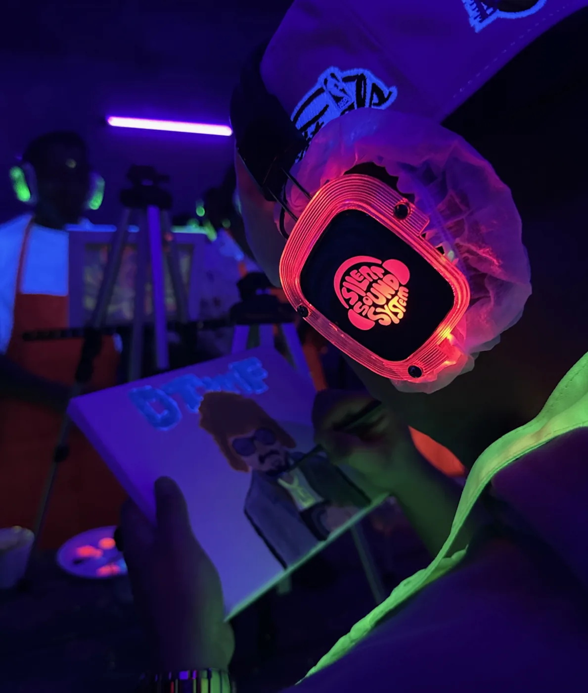 A guest wearing glowing wireless headphones at a Tropikal silent painting experience